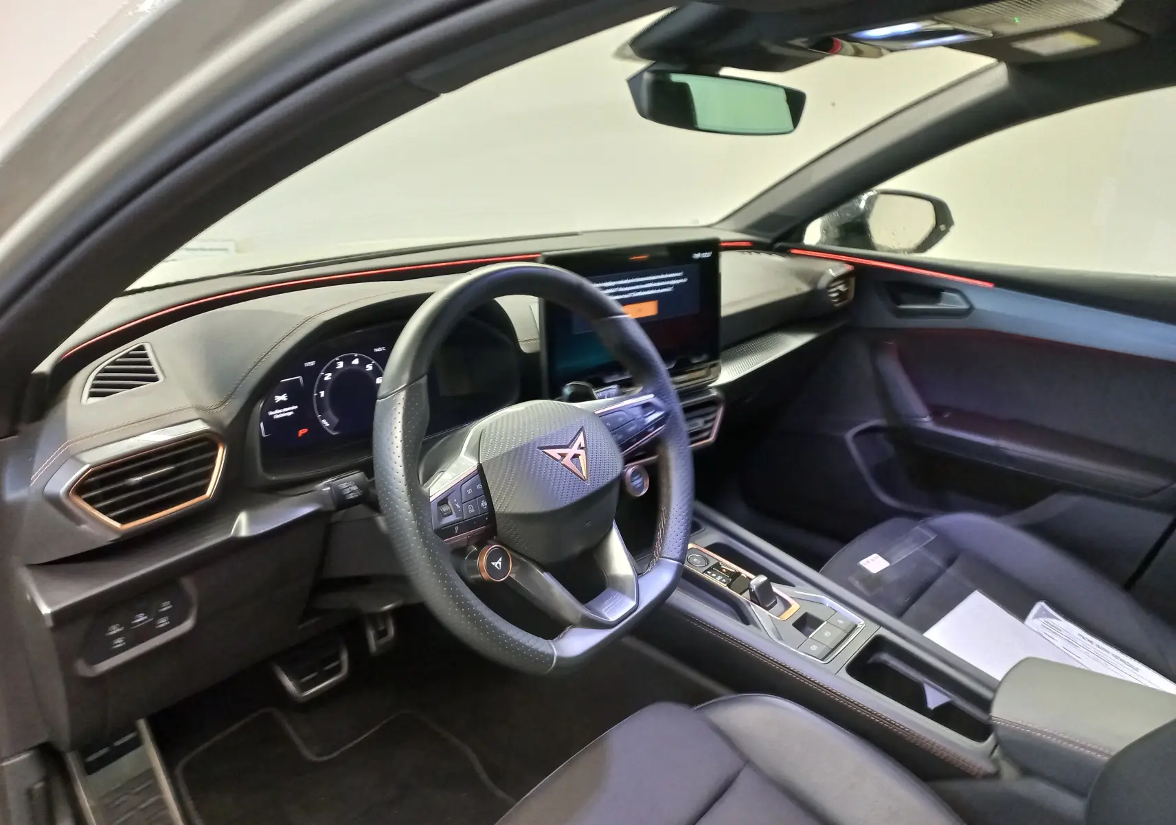 Vue intérieure côté conducteur du CUPRA LEON ST 1.5 eTSI 2025, avec éclairage d'ambiance rouge et tableau de bord digital.