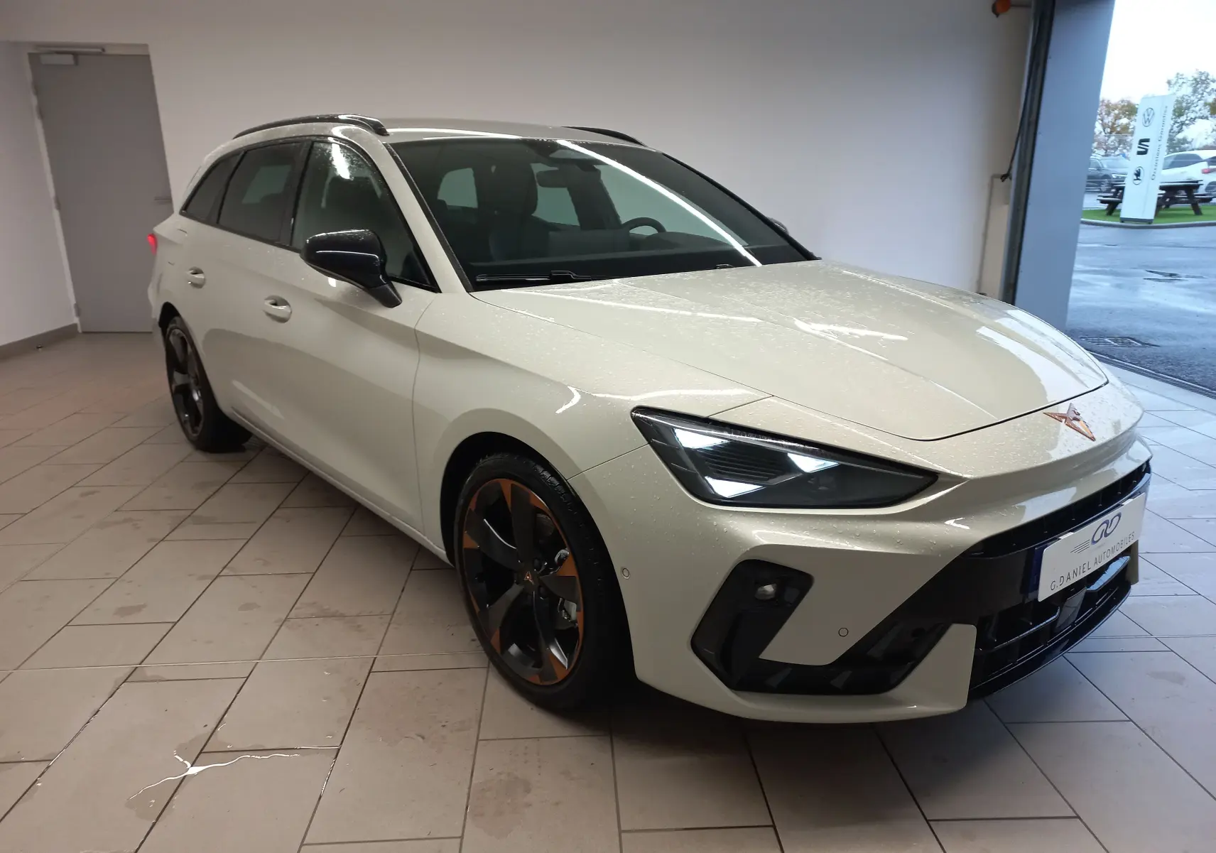Vue 3/4 avant d'une CUPRA Leon ST 1.5 eTSI 150 DSG7 en gris Taiga avec jantes alliage 18'' cuivrées dans un garage.