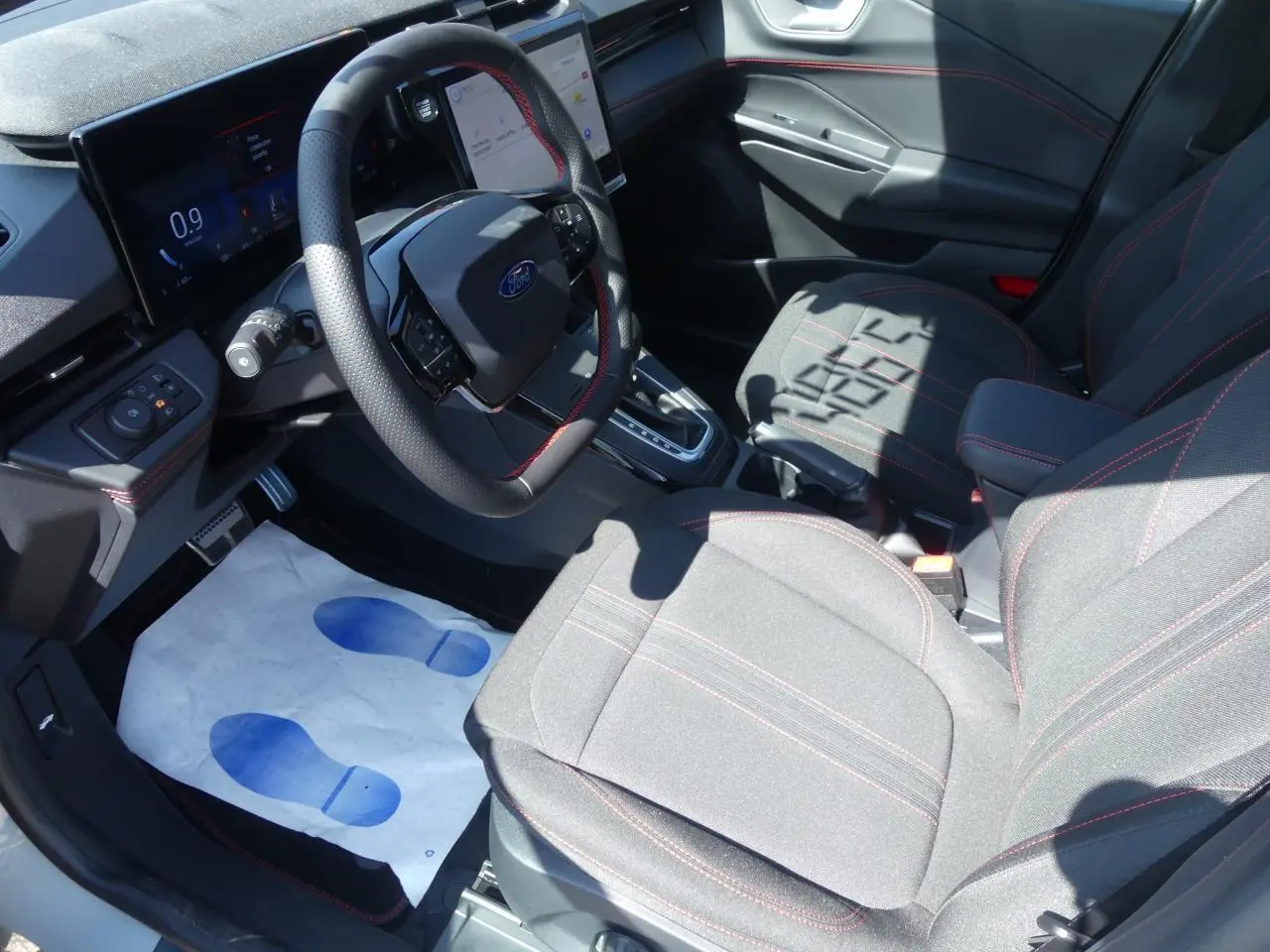 Intérieur Ford Puma 2025 vu côté conducteur, sièges tissu gris avec surpiqûres rouges et volant multifonction.