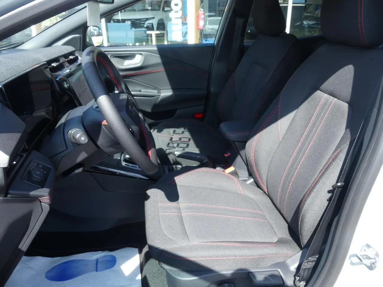 Intérieur avant droit du Ford Puma 2025, sièges tissu gris avec surpiqûres rouges et volant sport perforé.