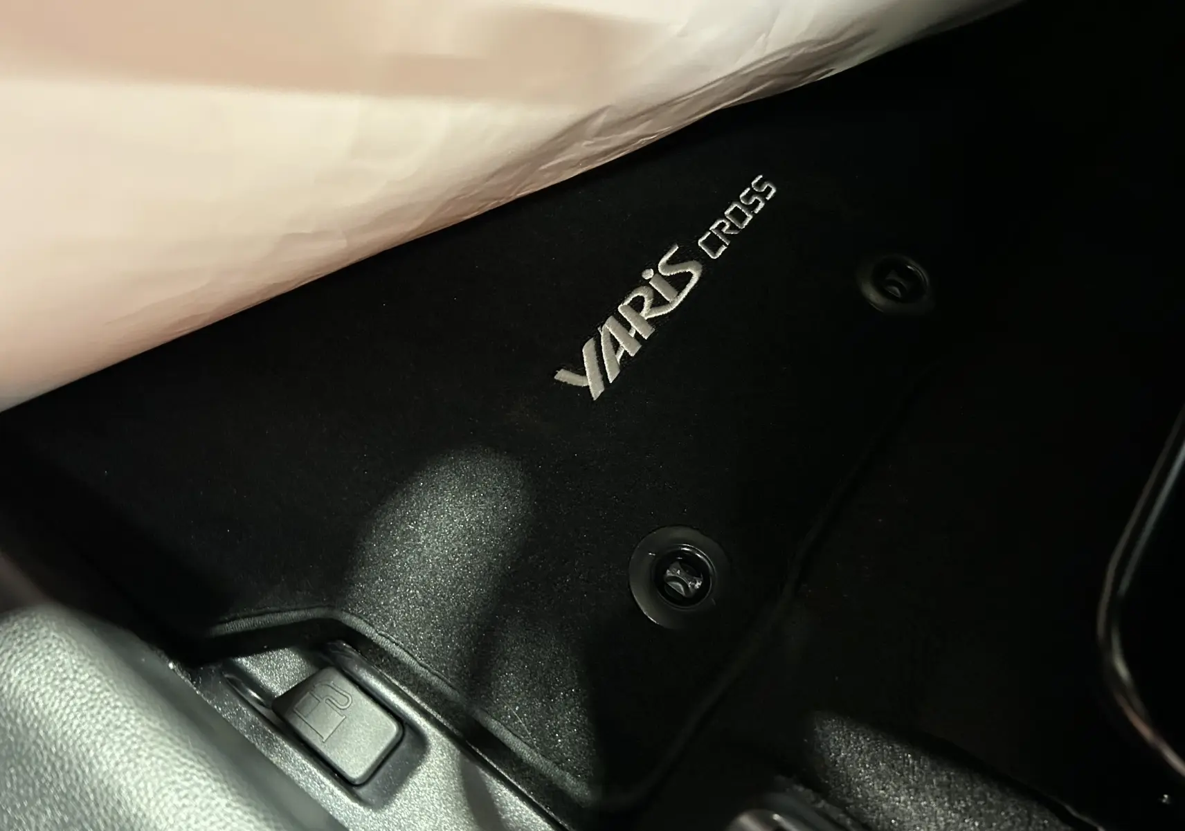 Détail du tapis de sol noir avec logo YARIS CROSS brodé, côté conducteur d'un Toyota Yaris Cross blanc 2025.