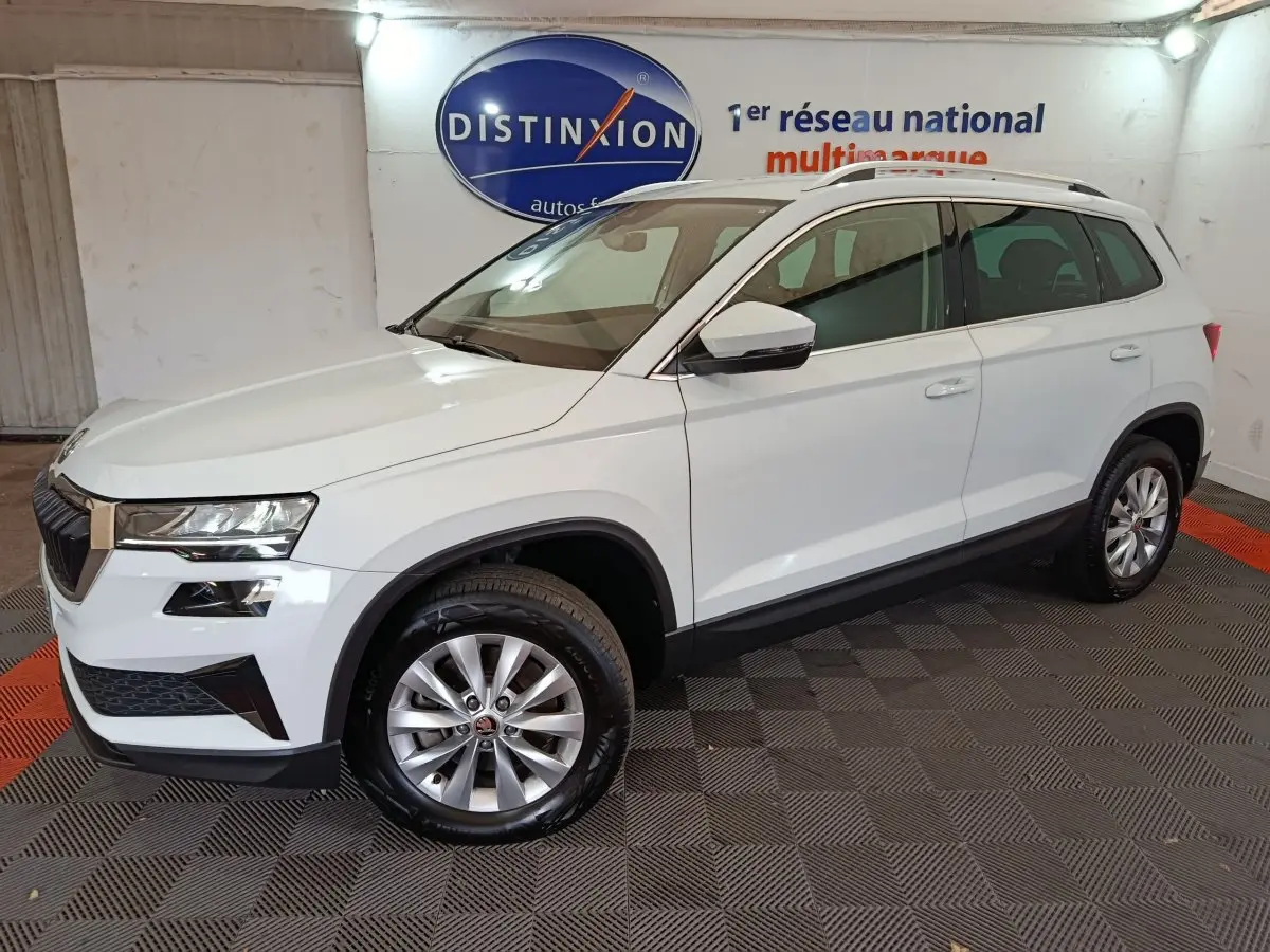 Vue 3/4 avant droite d'un Skoda Karoq blanc 2024 avec jantes alliage et barres de toit noires en showroom