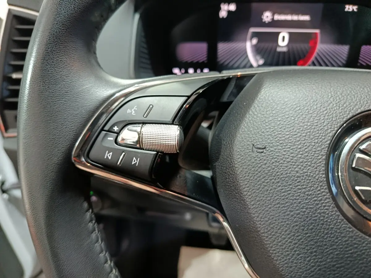 Gros plan sur la partie gauche du volant cuir noir du Skoda Karoq 2024 avec commandes audio et affichage numérique en arrière-plan.