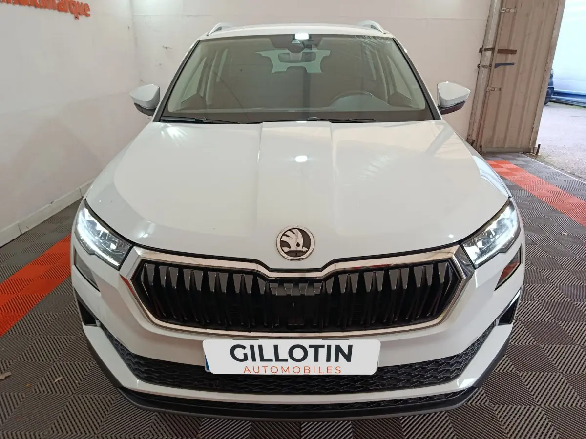 Vue avant d'un Skoda Karoq blanc avec calandre noire et phares LED allumés en intérieur showroom.