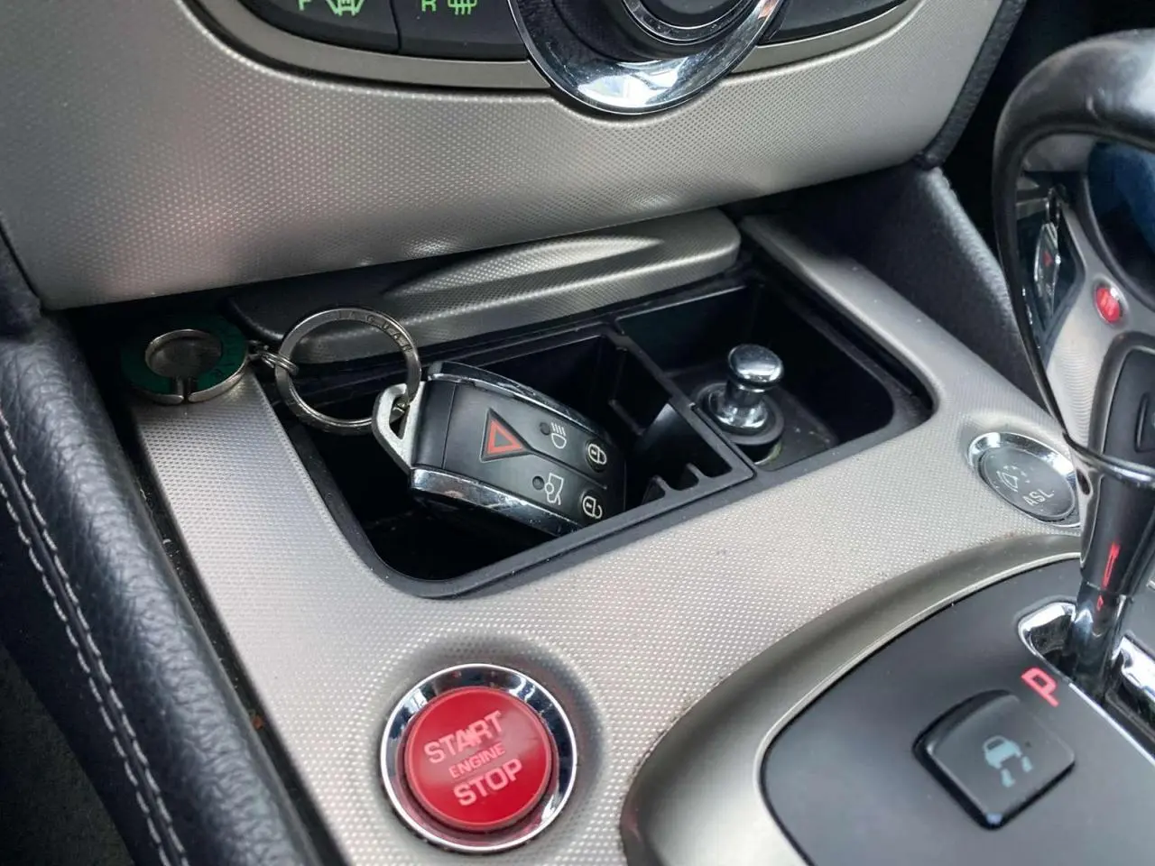 Gros plan sur la console centrale gris clair du Jaguar XK 2009 avec bouton start/stop rouge et clé dans le rangement.