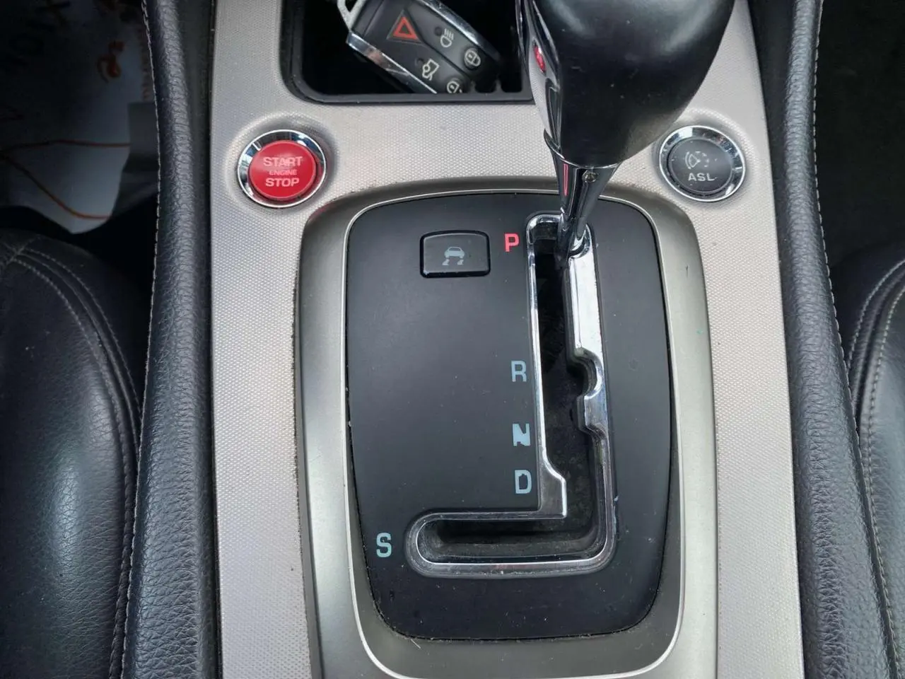 Gros plan sur la console centrale de la Jaguar XK 2009, levier de boîte auto et bouton rouge Start/Stop visibles.