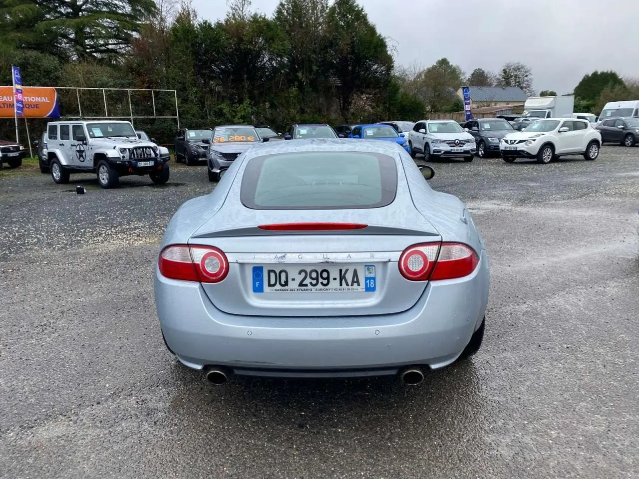 Vue arrière d'une Jaguar XK Coupé gris clair de 2009 avec feux ronds et double sortie d'échappement visible.