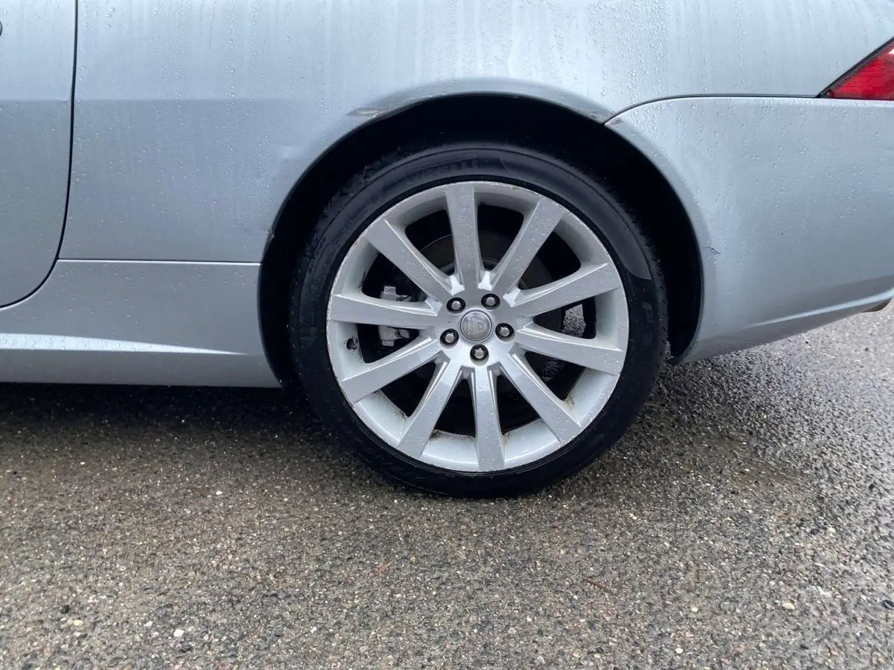 Gros plan sur la roue arrière droite gris clair d'une Jaguar XK Coupé 4.2i V8 de 2009 sous la pluie.