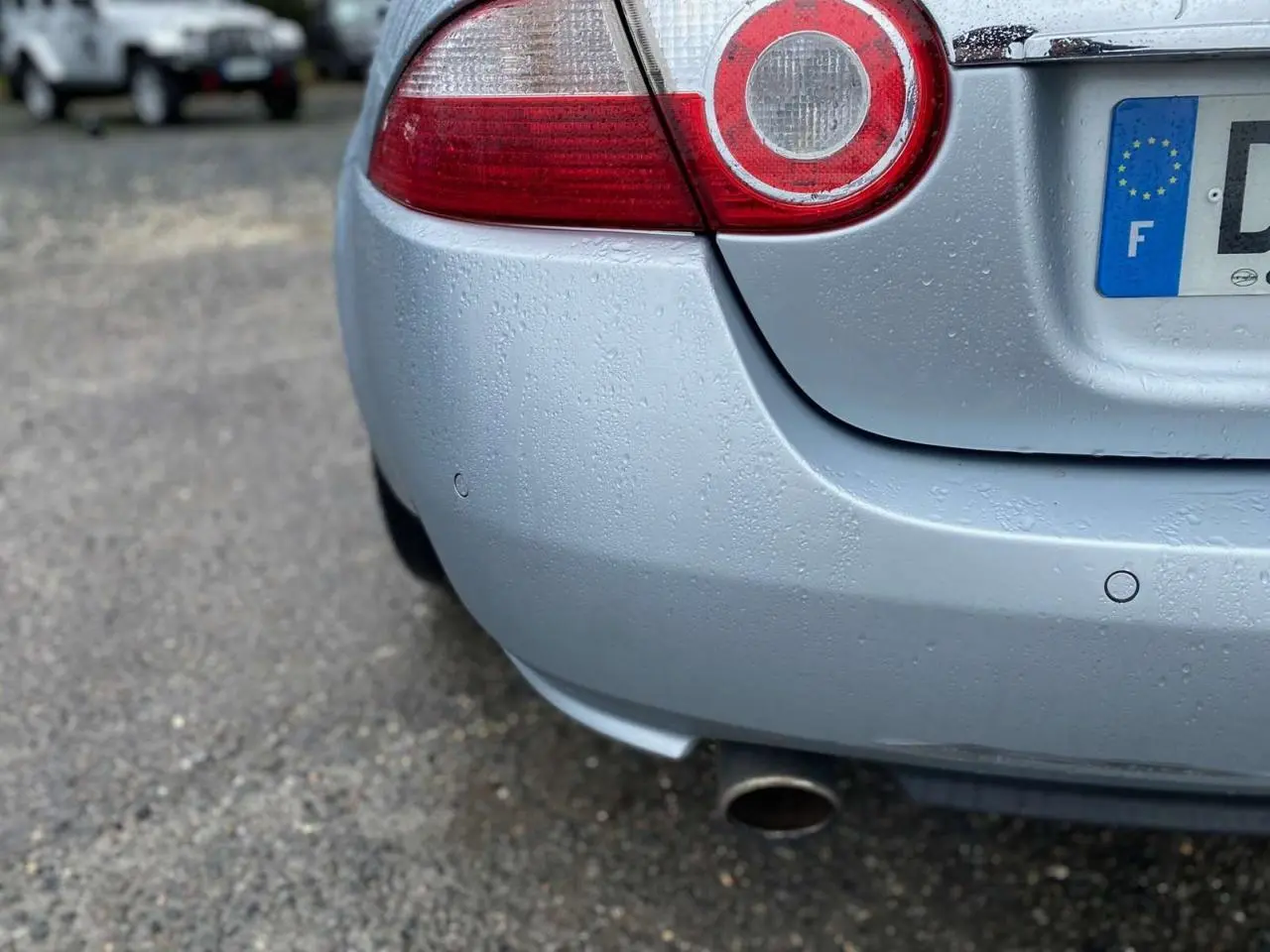 Gros plan sur l'arrière droit gris clair d'une Jaguar XK 4.2i V8 2009 avec feu rond et sortie d'échappement visible.
