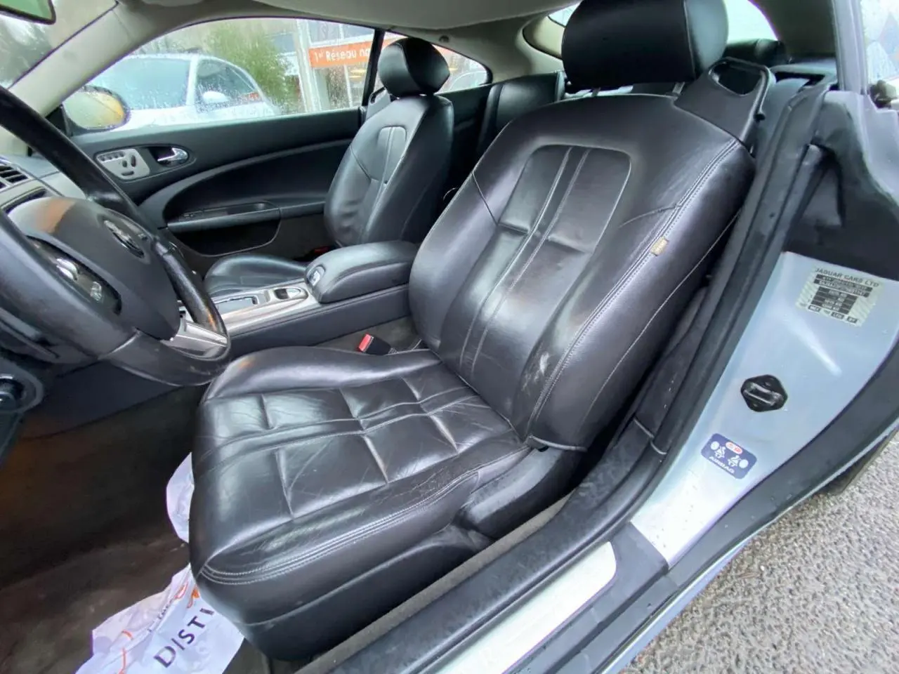 Vue intérieure côté conducteur de la Jaguar XK Coupé gris clair 2009, sièges en cuir noir et console centrale visible.