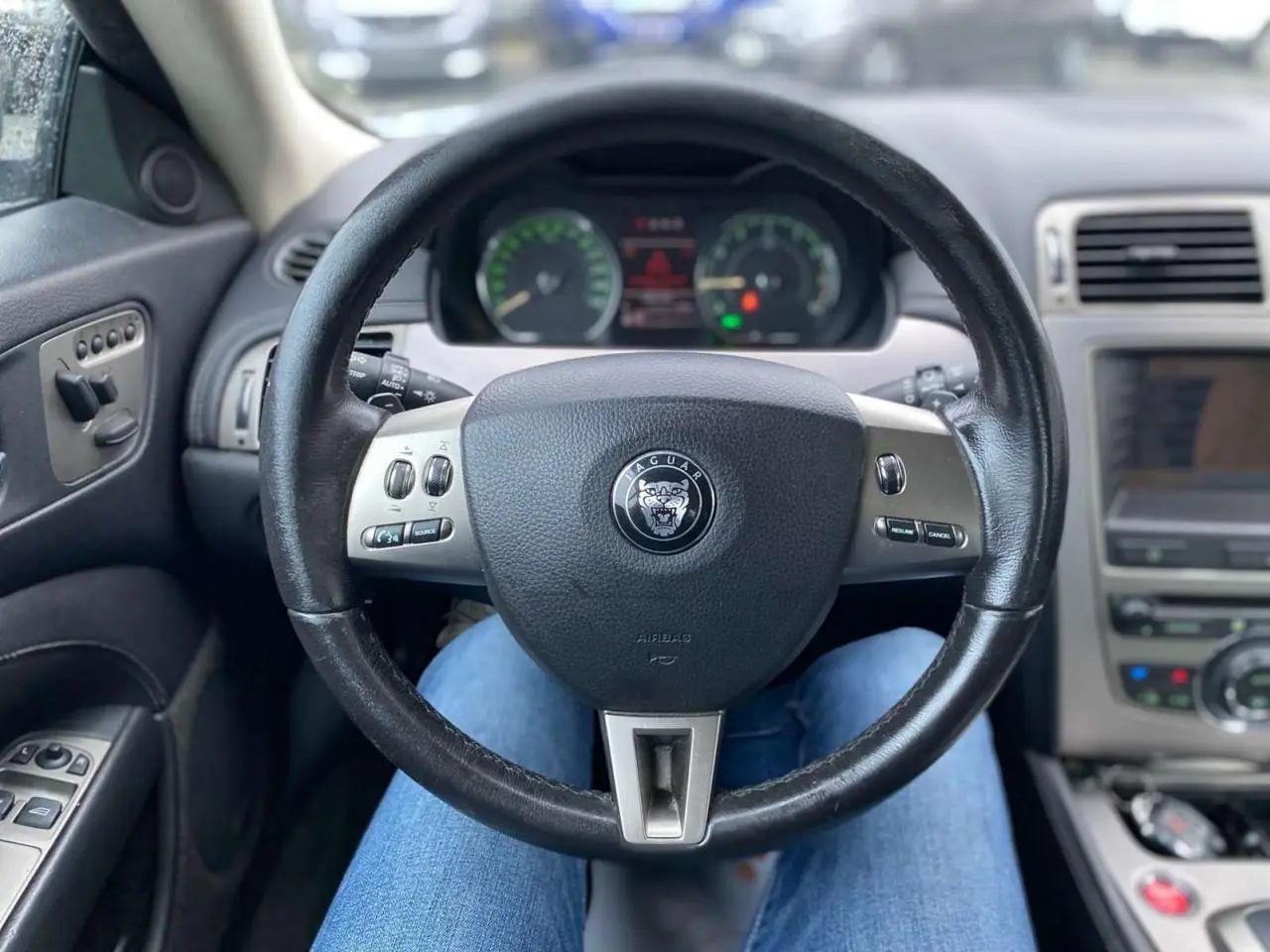 Vue intérieure centrée sur le volant noir de la Jaguar XK 4.2i V8 2009 avec commandes intégrées et tableau de bord flou.