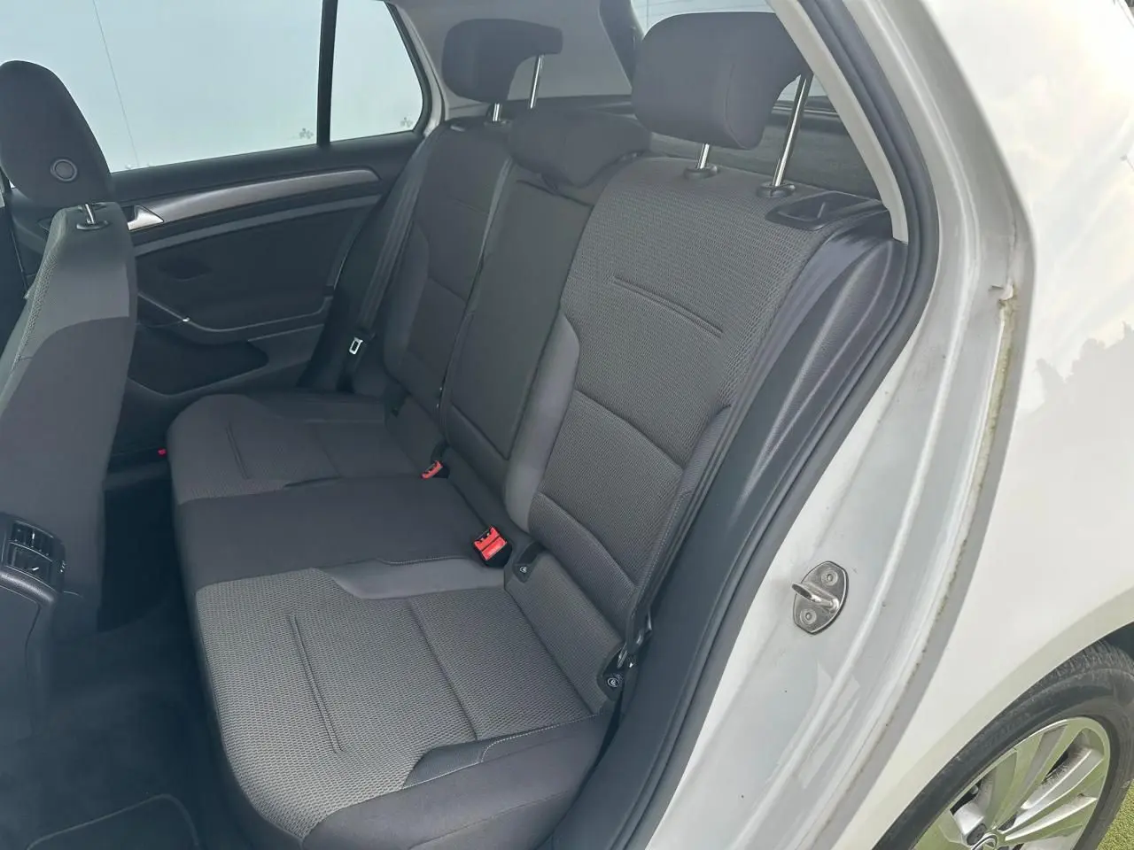 Vue côté droit de la banquette arrière grise de la Volkswagen Golf VII blanche avec appuie-têtes et ceintures de sécurité.