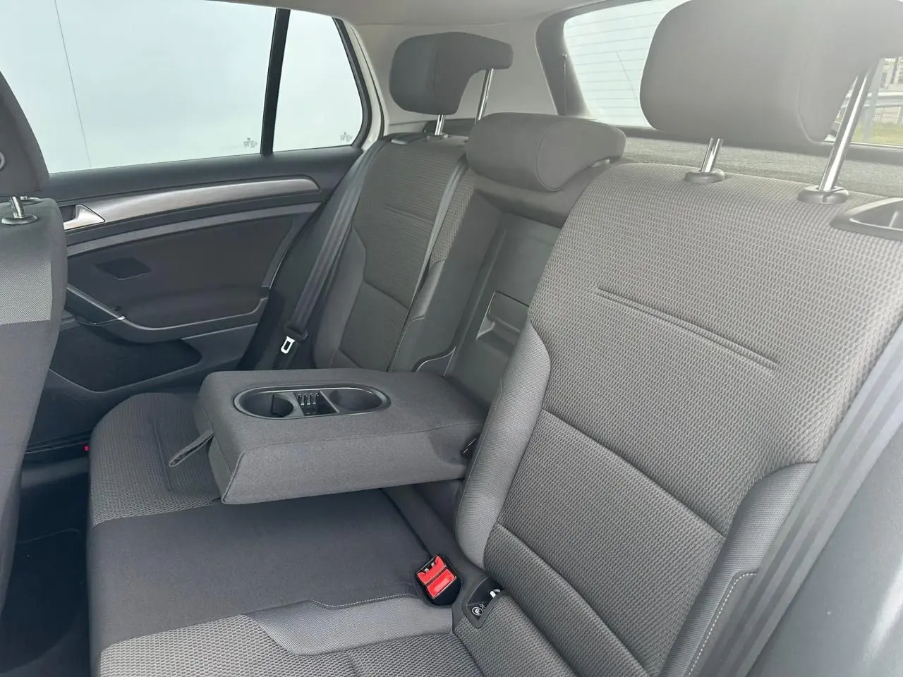 Vue intérieure côté droit de la banquette arrière grise avec accoudoir central relevé et porte-gobelets d'une Volkswagen Golf VII blanche.