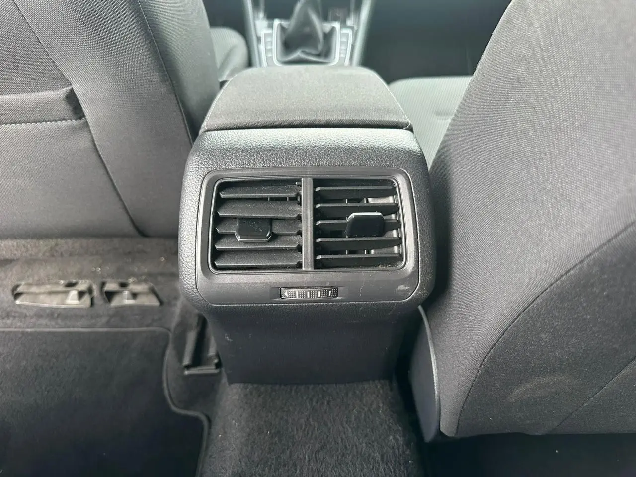 Gros plan sur les bouches d'aération arrière noires entre les sièges avant gris foncé d'une Volkswagen Golf VII blanche.
