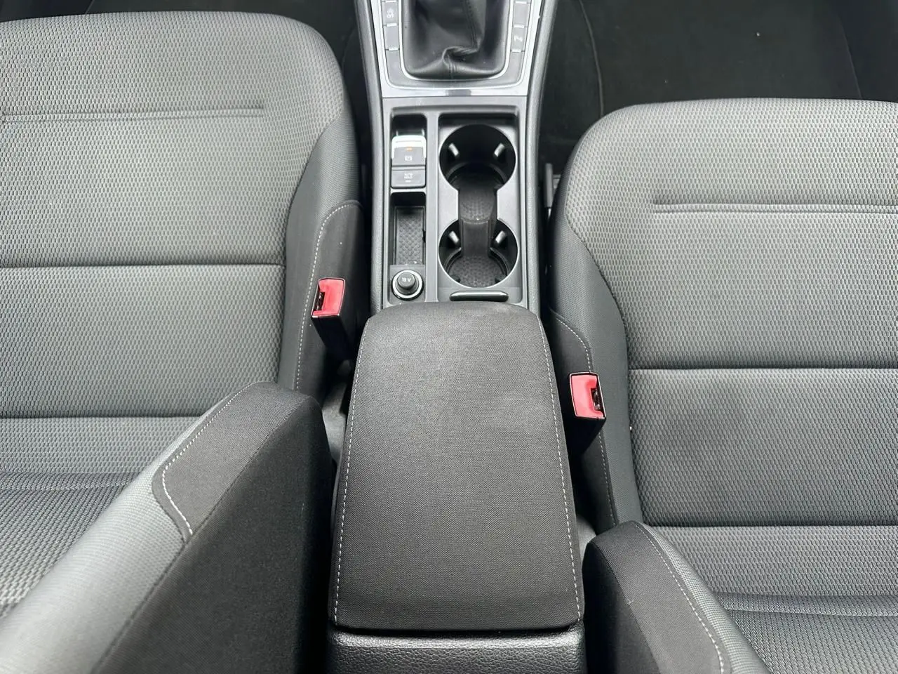 Vue plongeante sur l'accoudoir central noir et les sièges avant en tissu gris de la Volkswagen Golf VII blanche.