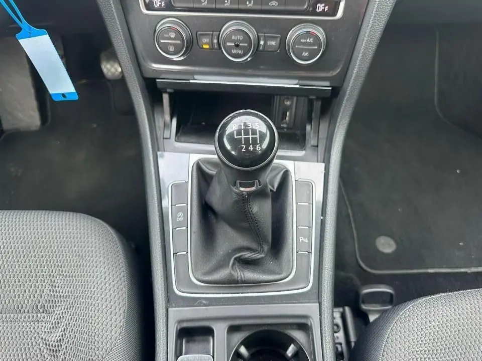 Vue rapprochée de la console centrale noire avec levier de vitesses manuel et sièges tissu gris d'une Volkswagen Golf blanche.