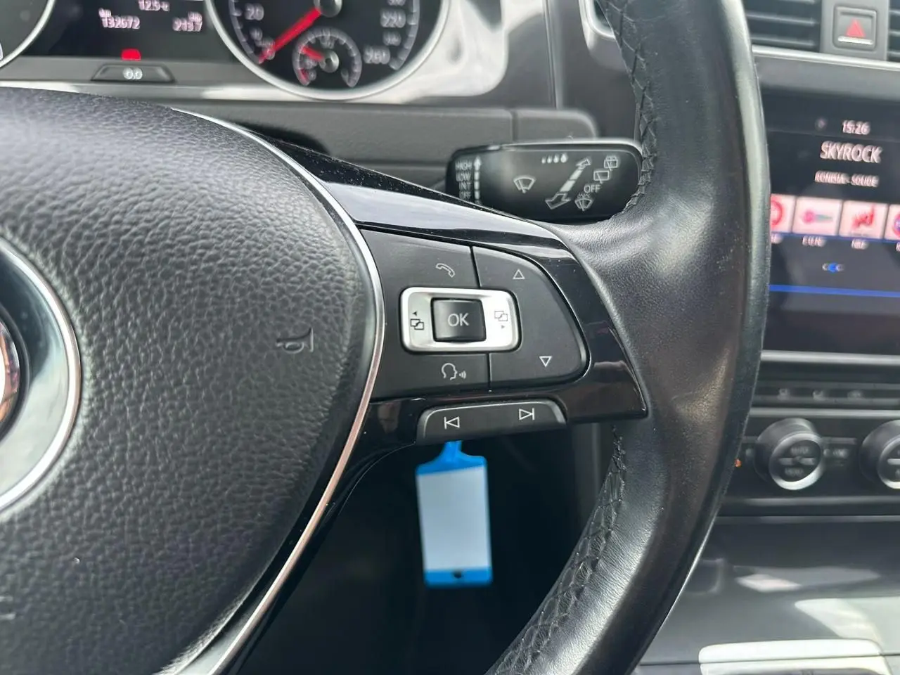 Gros plan sur le volant cuir côté gauche de la Volkswagen Golf blanche avec commandes multifonctions et tableau de bord visible.