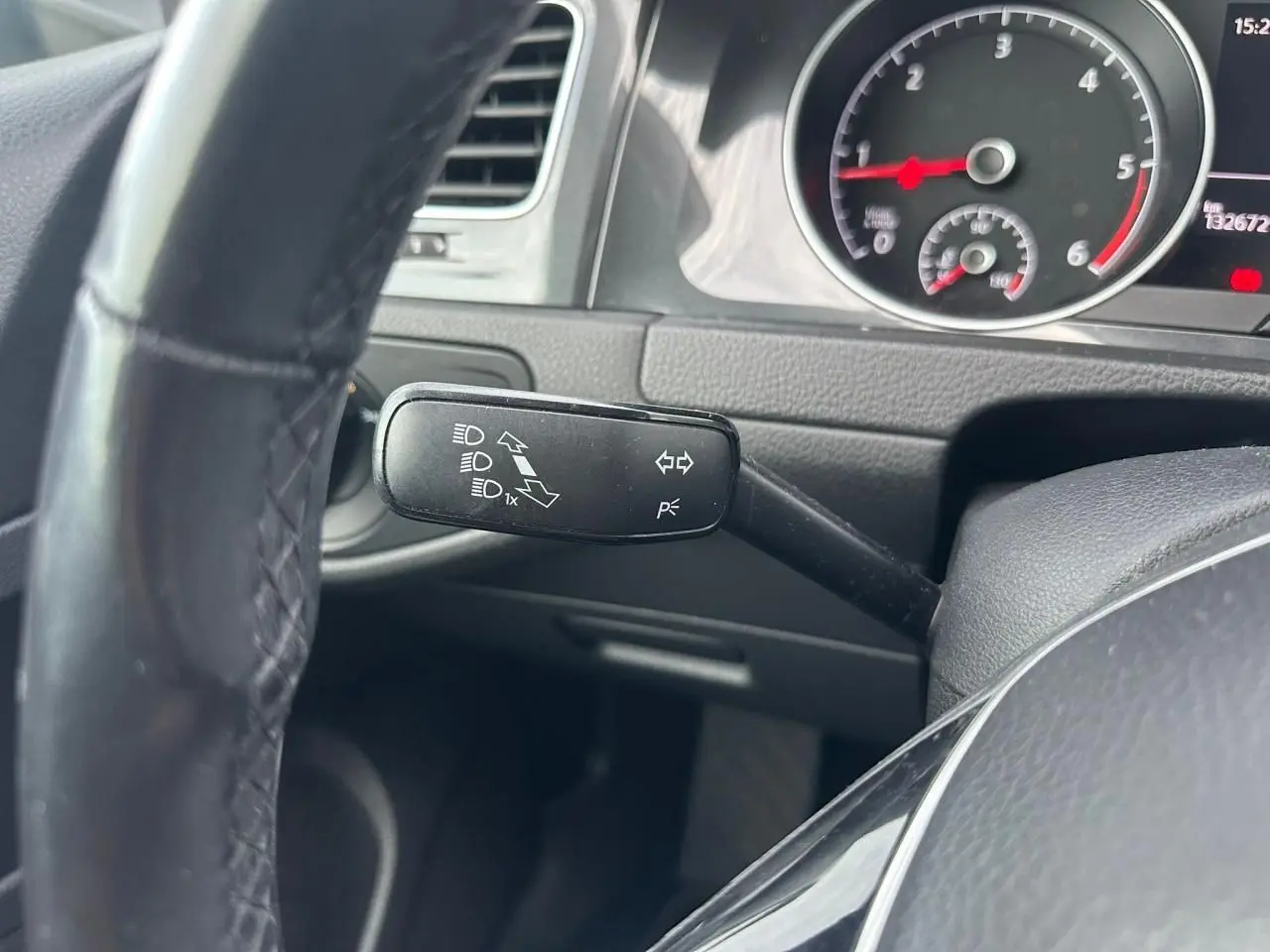 Gros plan sur la manette de clignotant à gauche du volant noir, avec tableau de bord et compte-tours visibles.