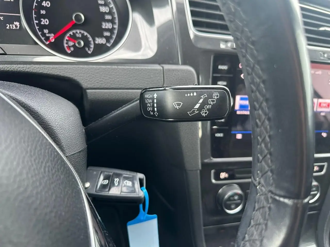 Gros plan sur le commodo d’essuie-glace à gauche du volant en cuir d’une Volkswagen Golf blanche, tableau de bord visible.