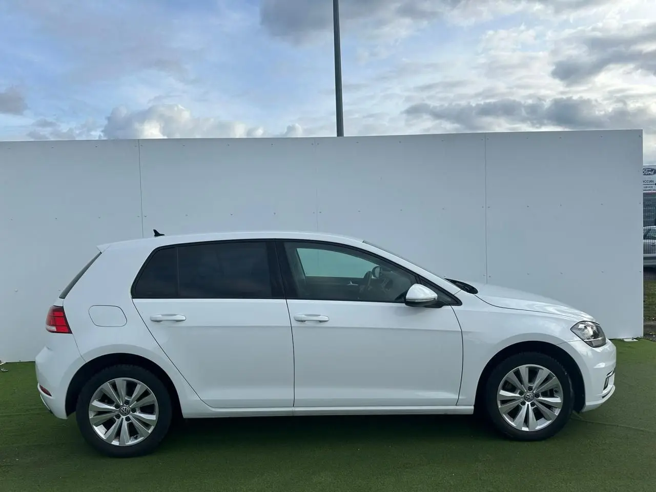Vue de profil côté gauche d'une Volkswagen Golf VII blanche sur fond neutre extérieur.