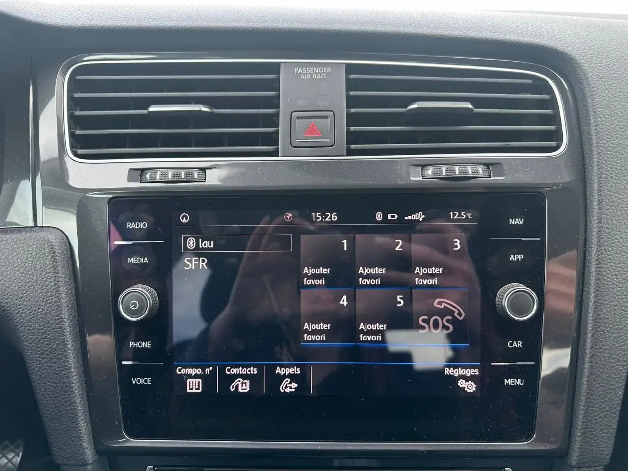 Vue rapprochée de l'écran tactile central noir du système multimédia d'une Volkswagen Golf blanche, avec commandes autour.
