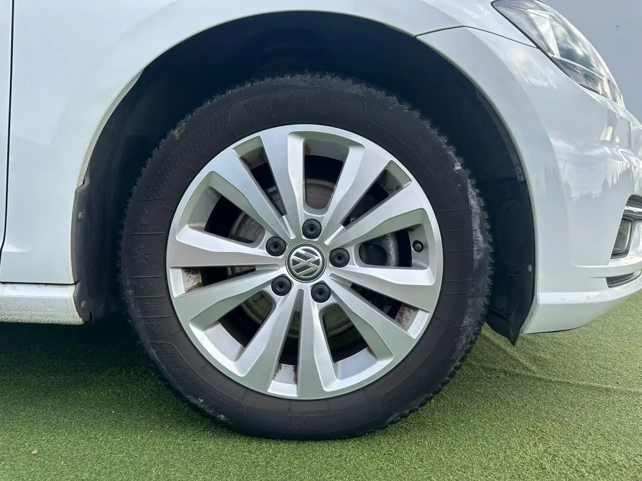 Gros plan sur la roue avant droite d'une Volkswagen Golf blanche, jante alliage 16 pouces au design moderne.