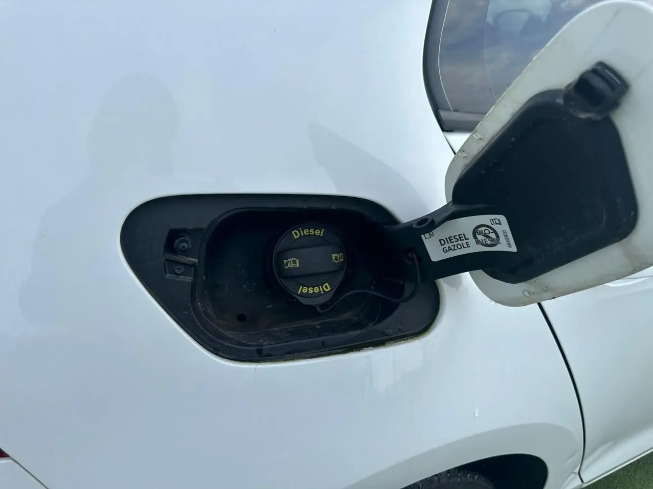Gros plan sur la trappe à carburant ouverte d’une Volkswagen Golf blanche, bouchon diesel visible côté arrière droit.