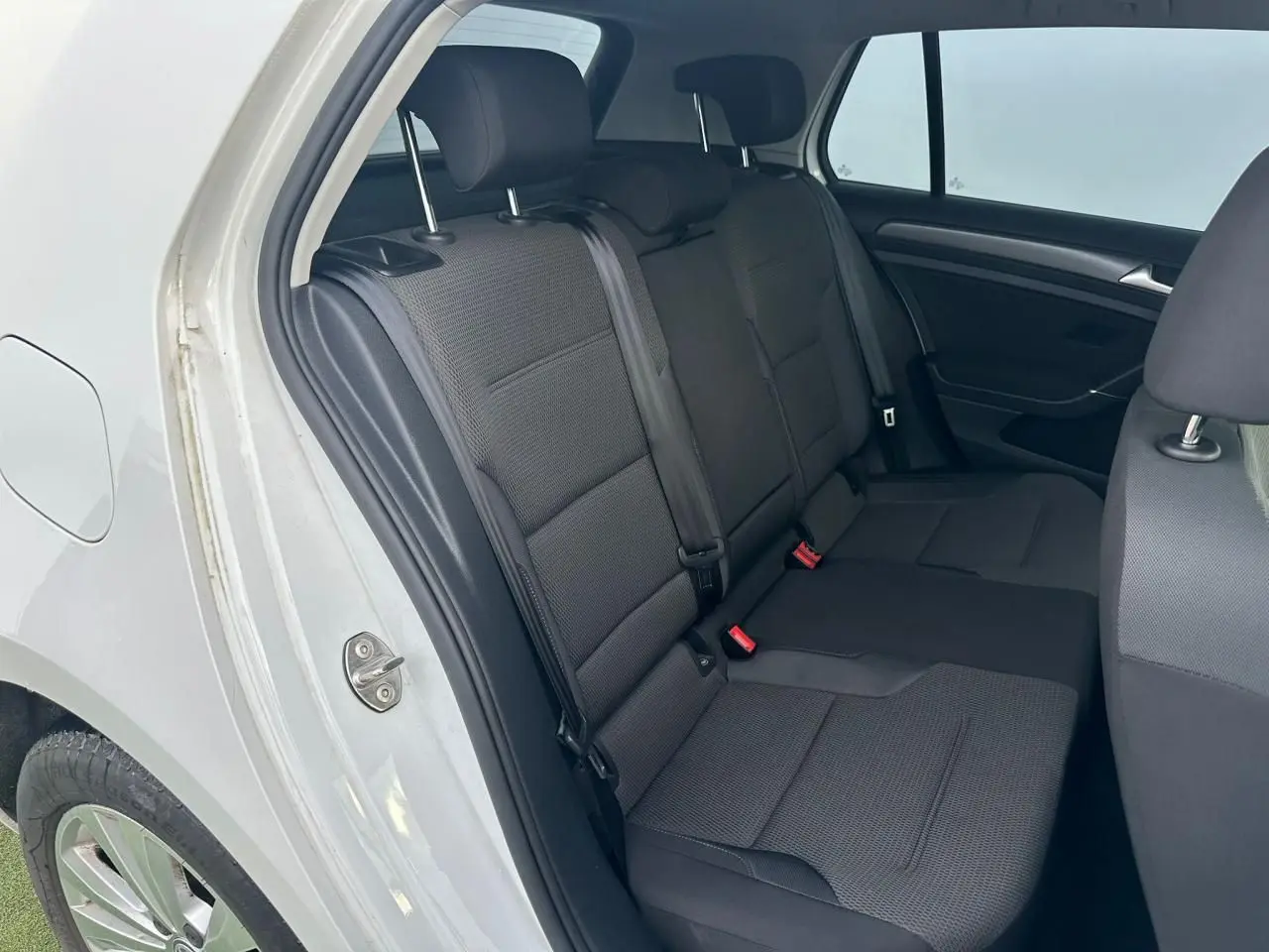 Vue intérieure côté arrière droit montrant la banquette noire et les ceintures de sécurité d'une Volkswagen Golf blanche.