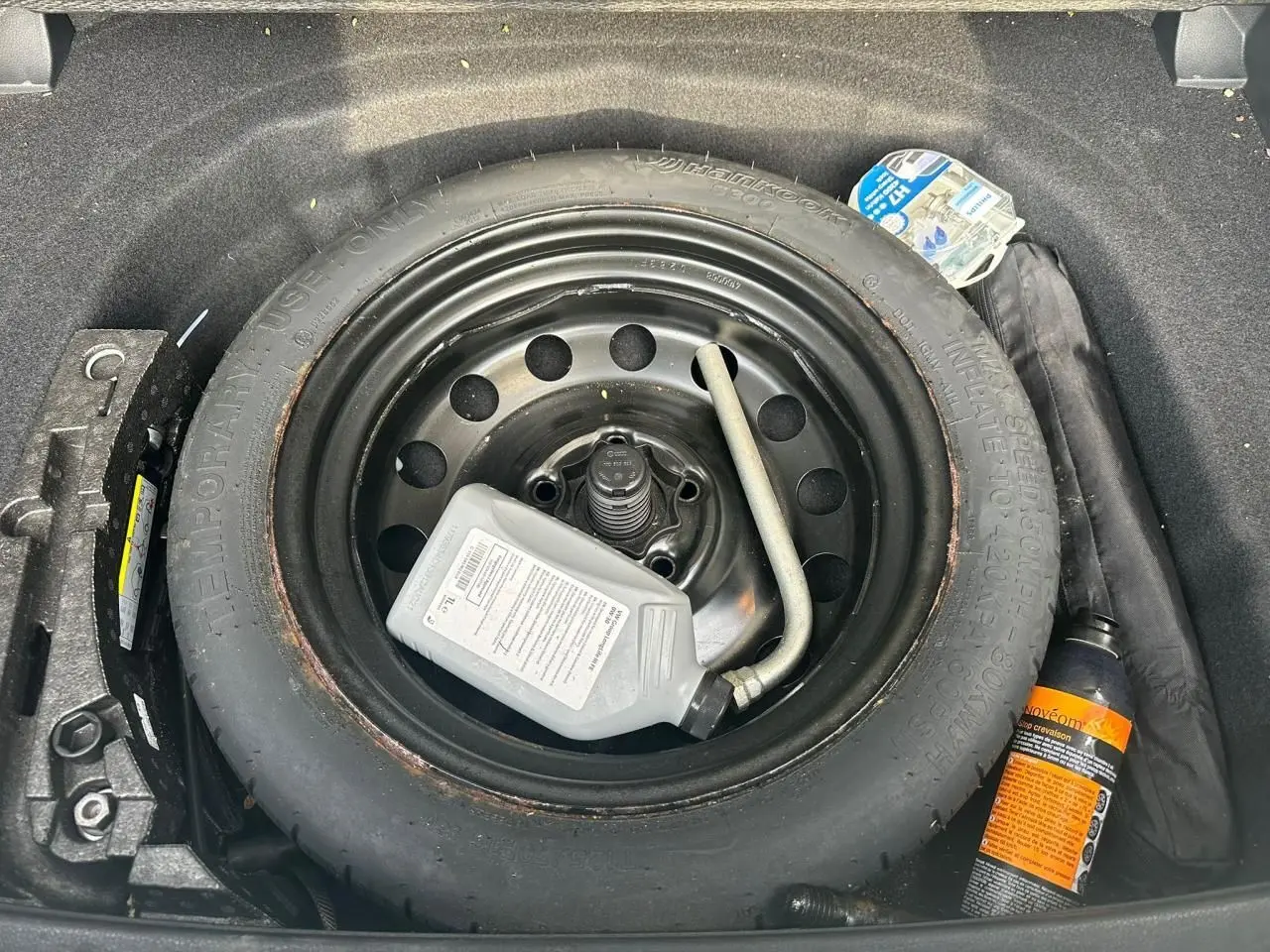 Vue plongeante sur la roue de secours noire dans le coffre d'une Volkswagen Golf blanche avec kit de réparation pneus.