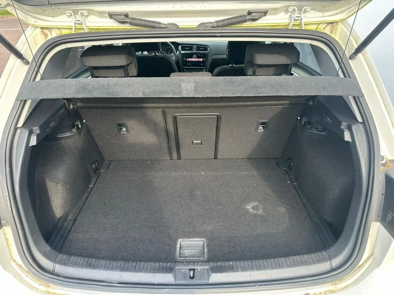 Coffre ouvert vu de l'arrière d'une Volkswagen Golf blanche, avec banquette arrière et tablette cache-bagages visibles.