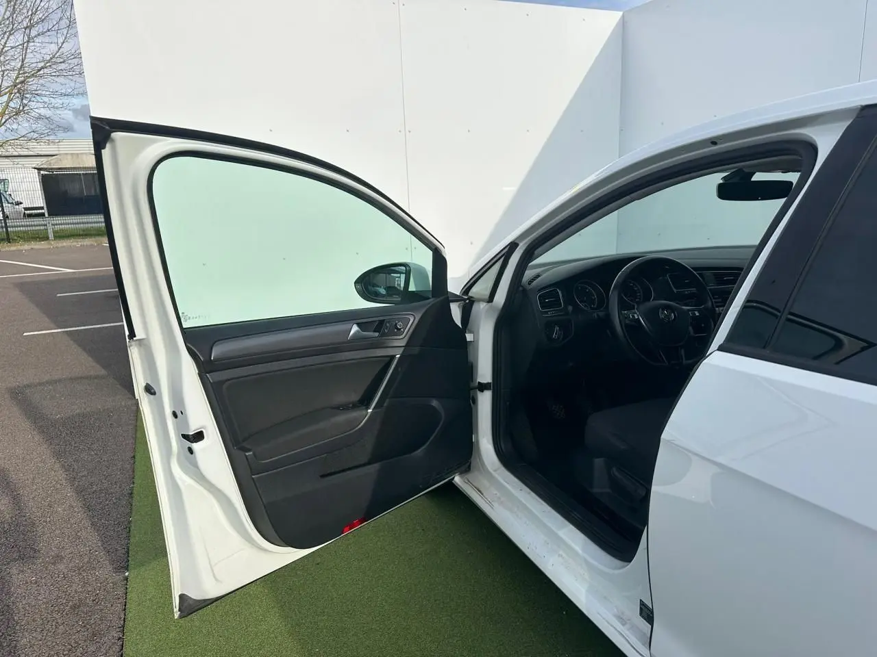 Vue côté gauche avant d'une Volkswagen Golf blanche 2018 avec porte ouverte dévoilant l'intérieur noir et le volant multifonction.