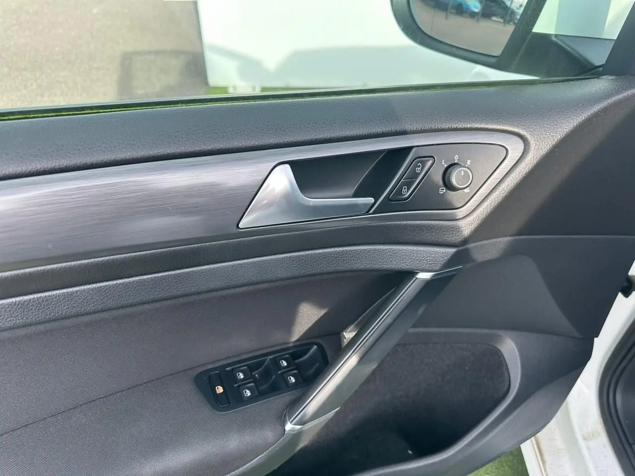Vue intérieure côté gauche de la porte avant d’une Volkswagen Golf blanche, avec commandes de vitres et rétroviseurs.