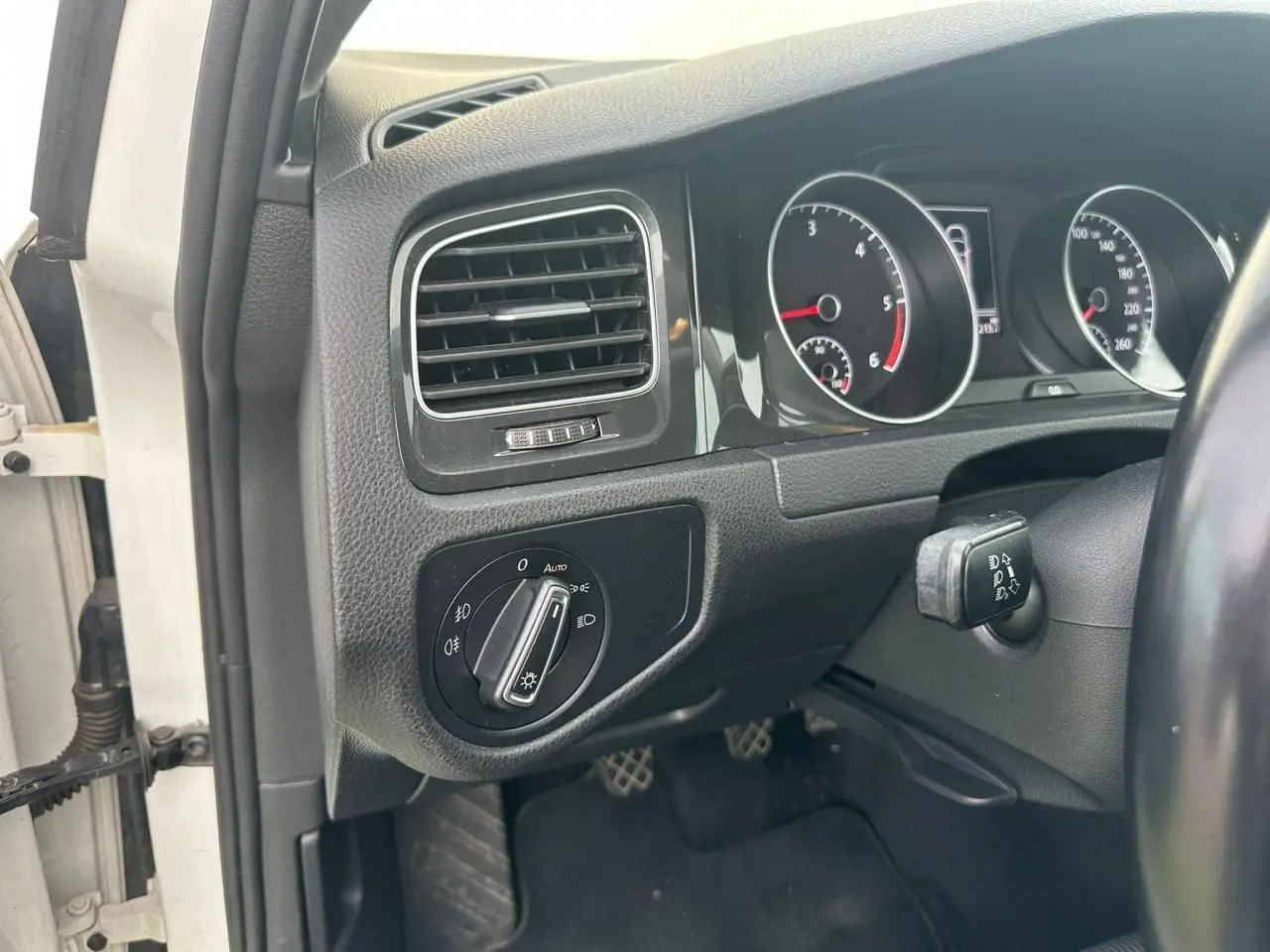 Vue intérieure côté gauche du tableau de bord noir d'une Volkswagen Golf blanche avec commandes d'éclairage et compteurs.