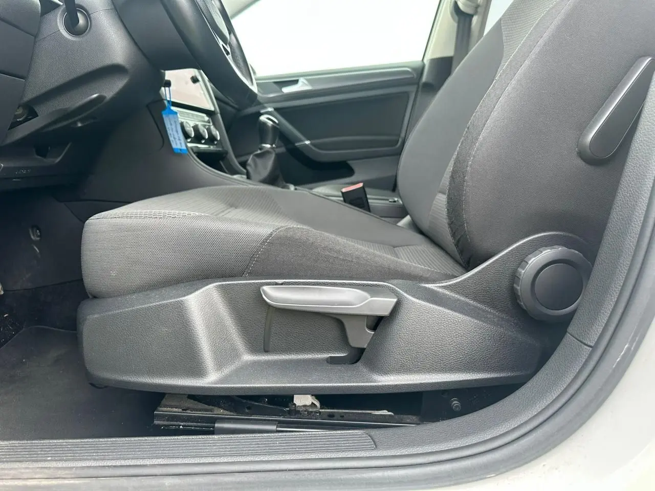 Vue intérieure côté conducteur de la Volkswagen Golf blanche 2018, mettant en valeur le siège avant gris et la console centrale.