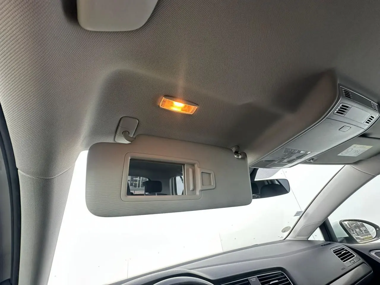 Vue intérieure côté conducteur de la Volkswagen Golf blanche, montrant le pare-soleil avec miroir éclairé et tableau de bord.