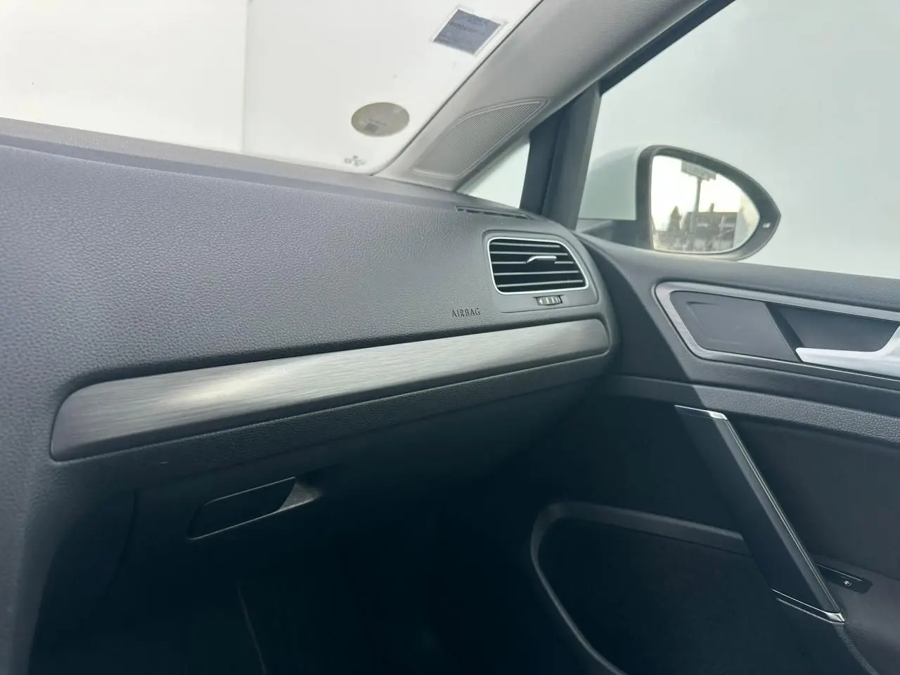 Vue intérieure côté passager avant de la Volkswagen Golf VII blanche, soulignant la planche de bord avec insert décoratif métal brossé.