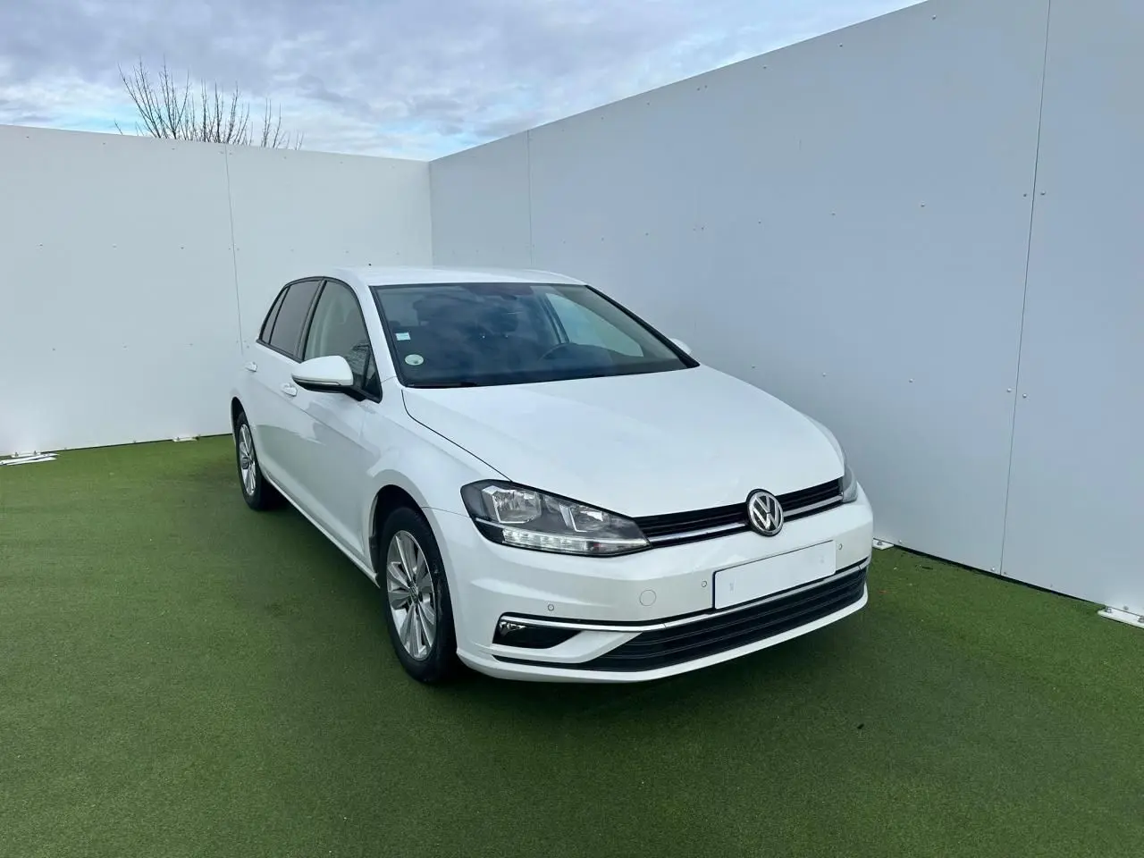 Volkswagen Golf VII blanche vue 3/4 avant droite sur sol vert avec pare-chocs et phares nets.
