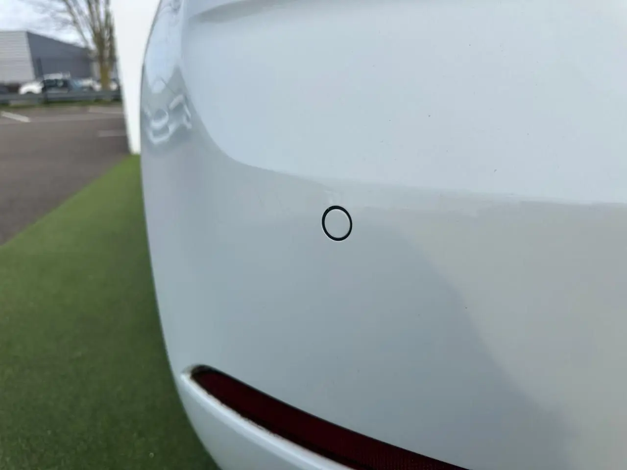 Gros plan sur le pare-chocs arrière blanc d'une Volkswagen Golf VII avec capteur de stationnement visible.