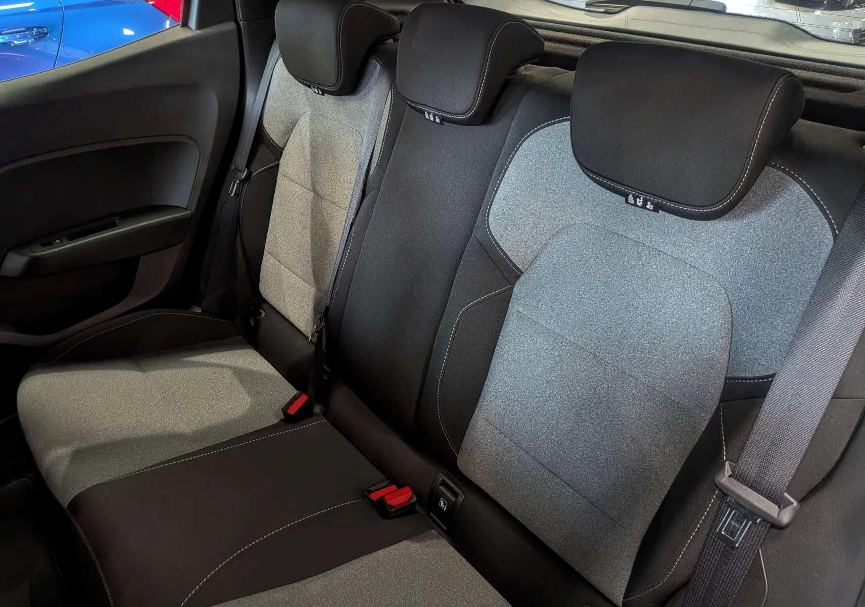 Vue intérieure des sièges arrière en tissu gris et noir de la Renault Clio V 2024, avec ceintures de sécurité visibles.