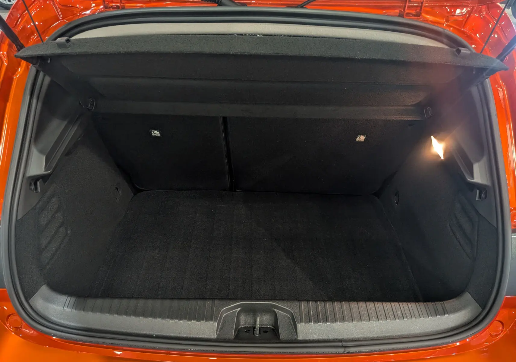 Coffre ouvert vu de l'arrière d'une Renault Clio V Orange Valencia, intérieur noir et éclairage latéral droit.