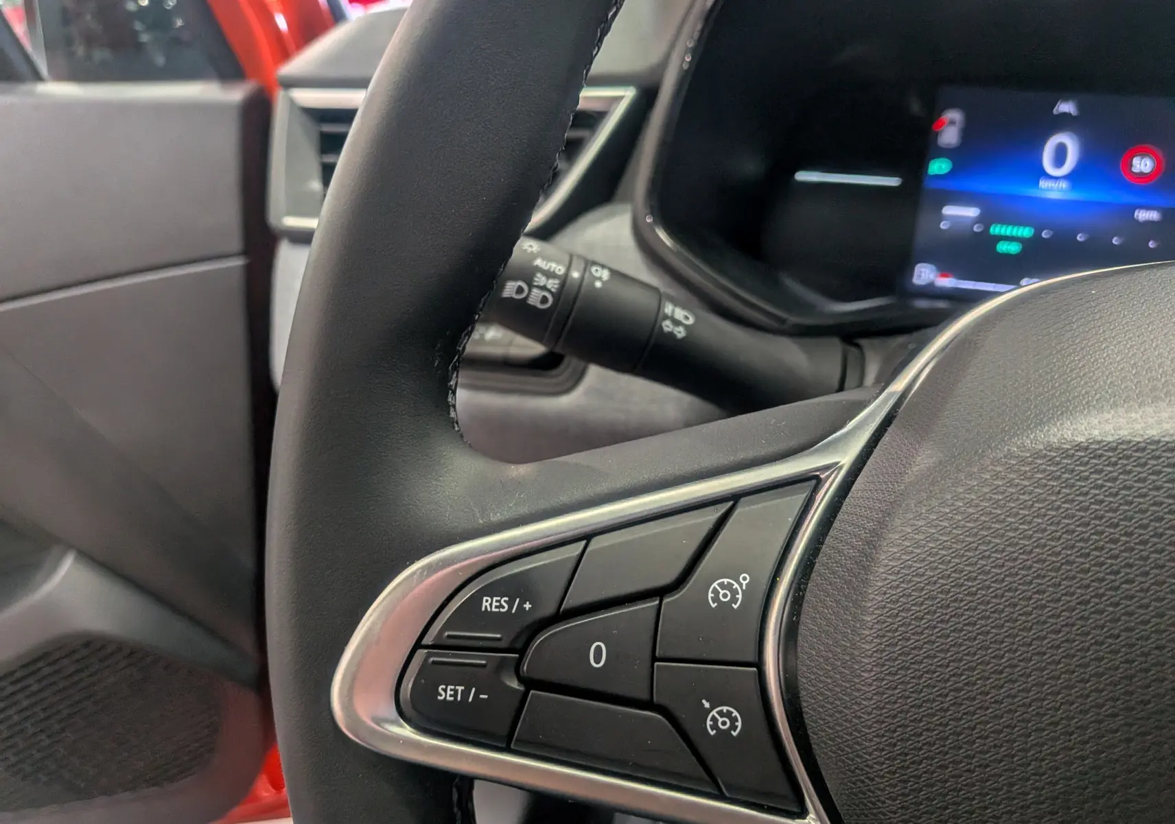 Gros plan sur le volant avec commandes de régulateur, tableau de bord numérique et intérieur orange Valencia de la Renault Clio V.