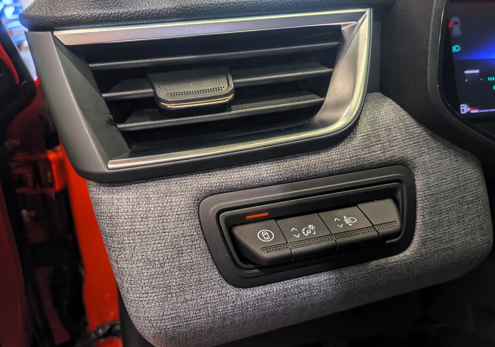 Détail du tableau de bord côté gauche de la Renault Clio V 2024, tissu gris avec commandes d’éclairage, porte orange Valencia visible.