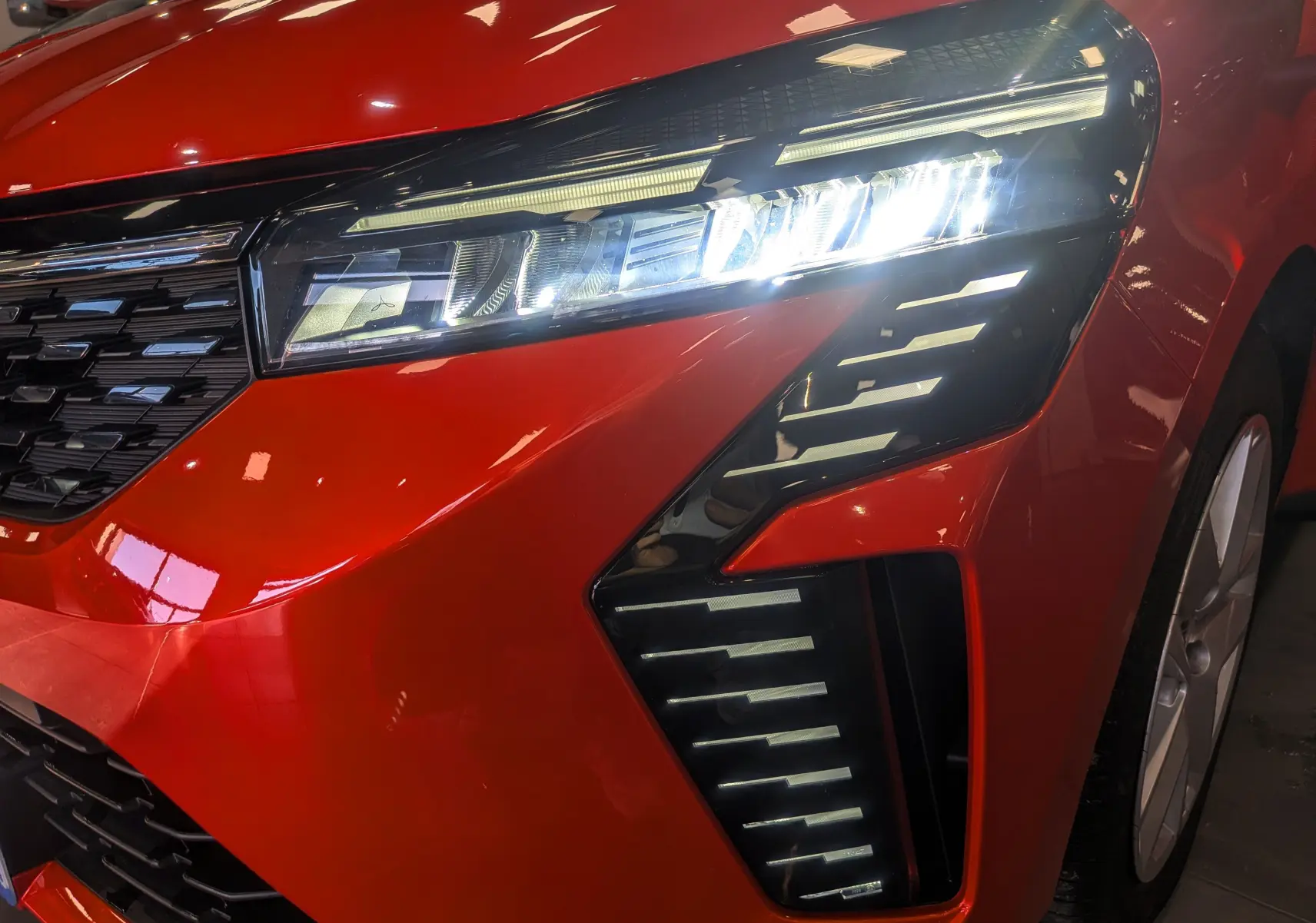 Gros plan sur l'avant droit orange Valencia de la Renault Clio V 2024, mettant en valeur le phare LED et la calandre noire.