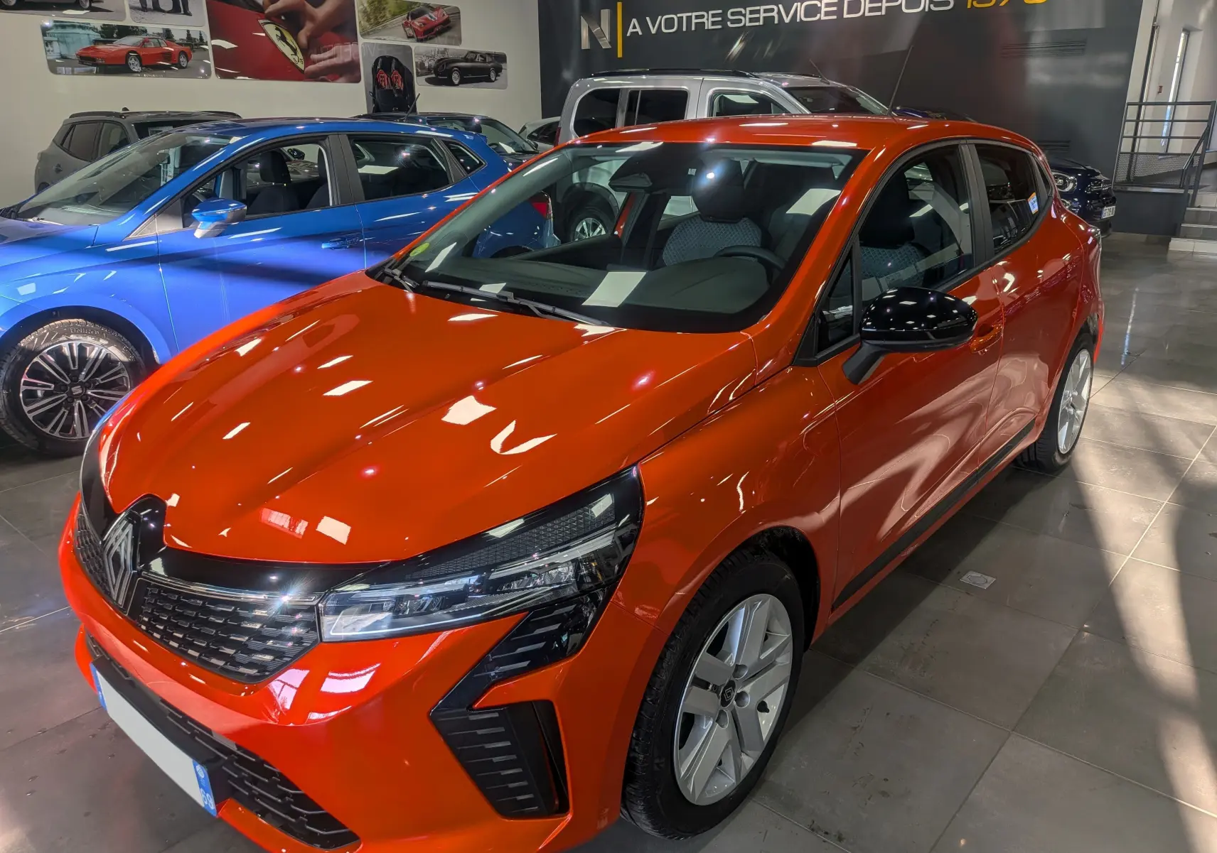 Renault Clio V Orange Valencia vue 3/4 avant droit en showroom, avec calandre noire et phares LED distinctifs.