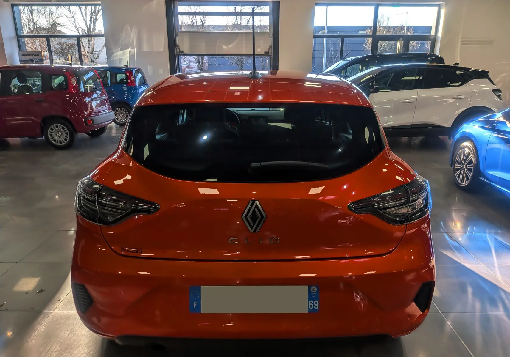 Vue arrière d'une Renault Clio V Orange Valencia 2024 dans un showroom, avec feux arrière LED et caméra de recul visible.