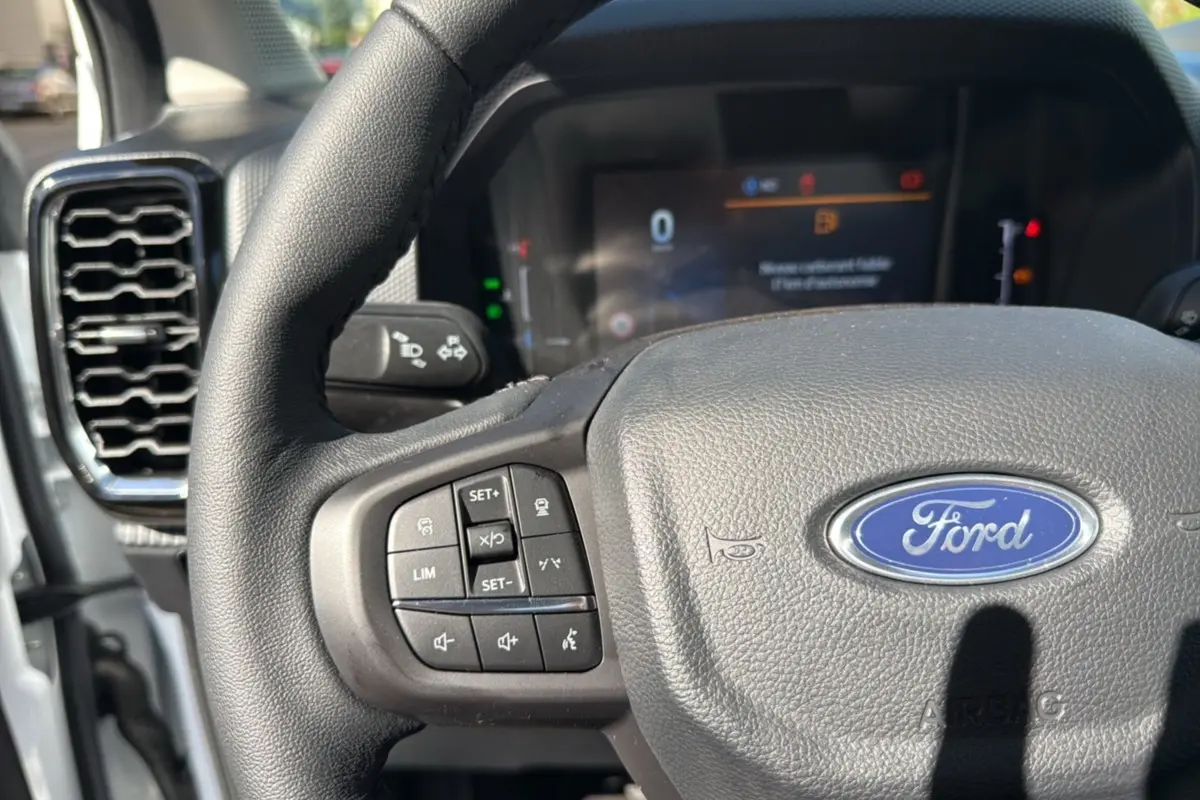 Gros plan sur le volant cuir multifonctions du Ford Ranger blanc glacier, avec tableau de bord numérique en arrière-plan flou.