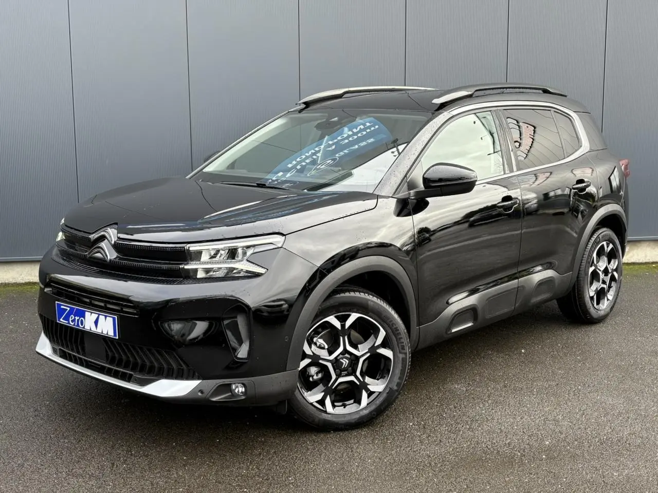 Vue 3/4 avant droite d'un Citroën C5 Aircross noir Perla avec jantes diamantées bi-ton et barres de toit noires.