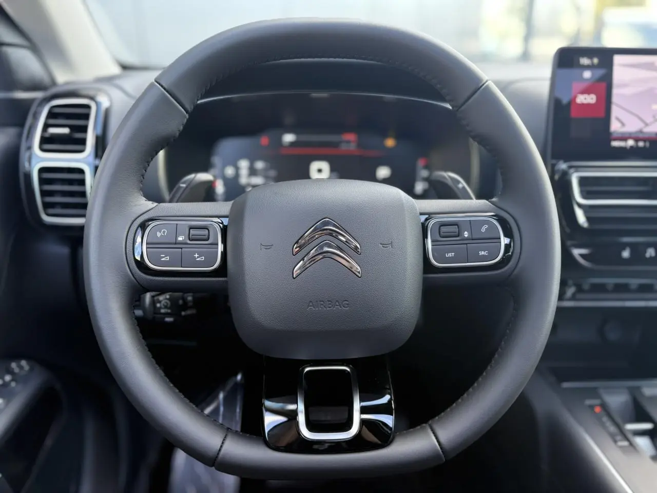 Vue rapprochée du volant noir en cuir du Citroën C5 Aircross 2025 avec commandes intégrées et tableau de bord numérique flou.