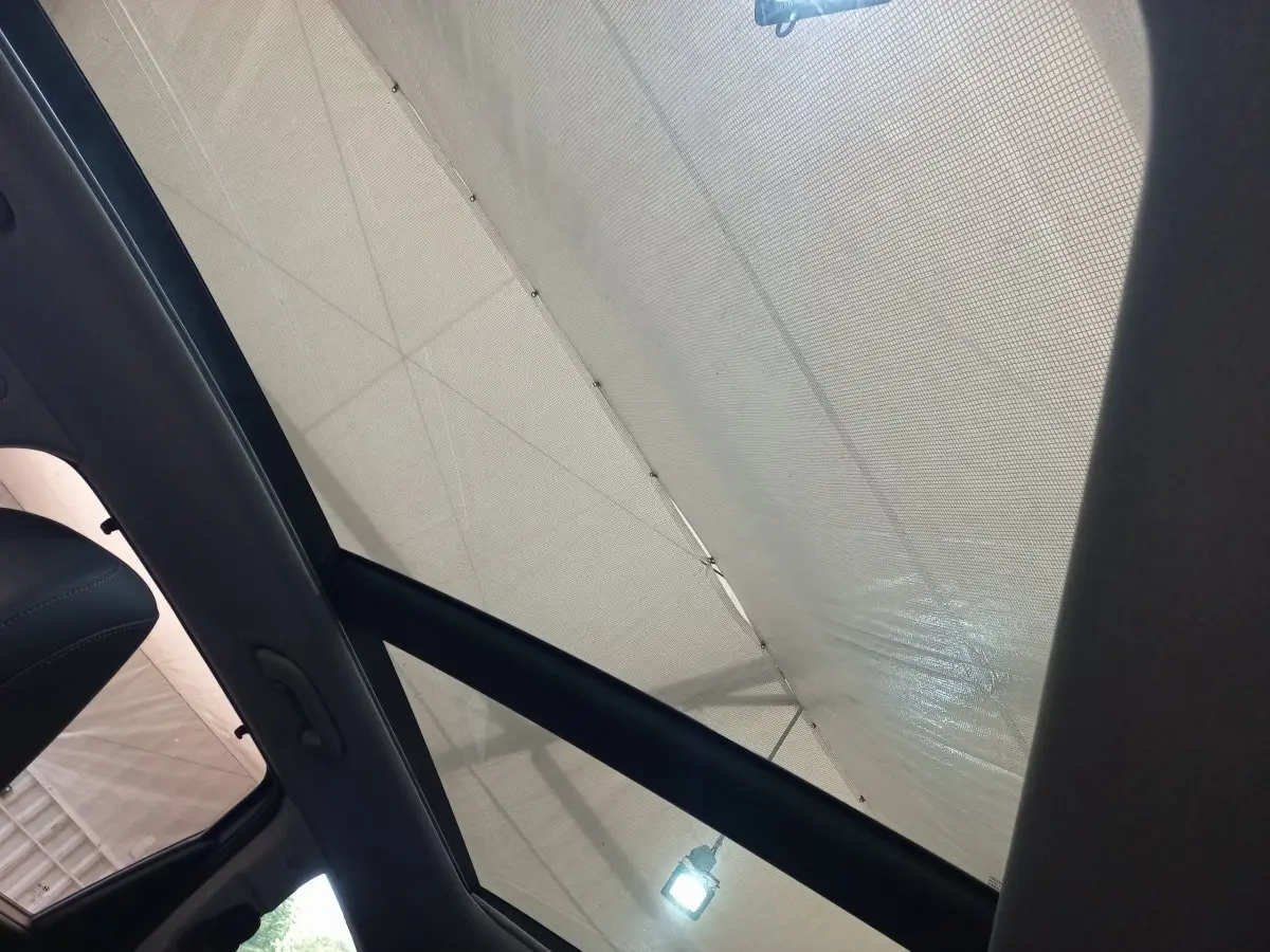 Toit ouvrant en verre incliné du Hyundai Santa Fe gris clair, vue intérieure vers le ciel couvert.