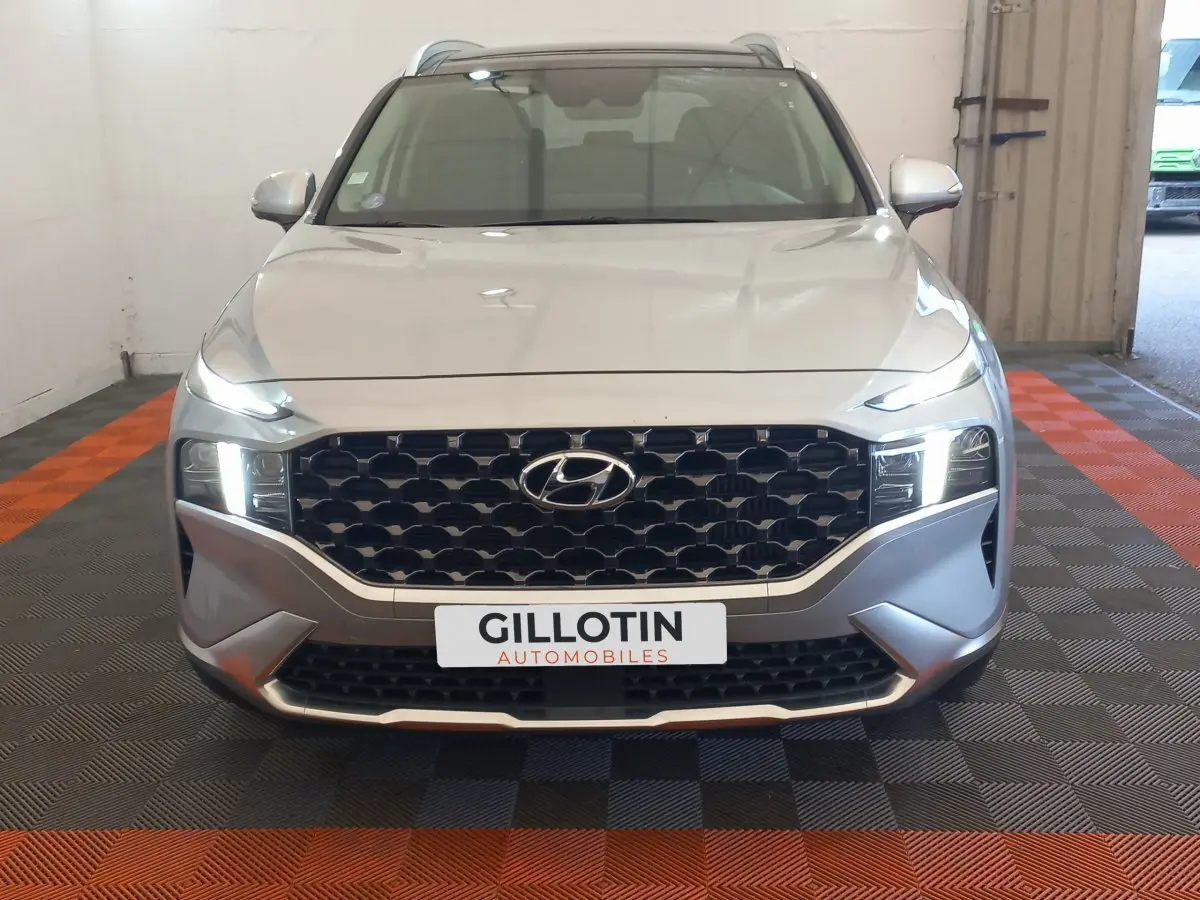 Vue avant d'un Hyundai Santa Fe gris clair avec calandre noire hexagonale et phares LED allumés.